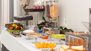 Uma mesa de buffet com diversos alimentos, incluindo frutas, pão e uma máquina de café.