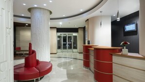 Una moderna zona de recepción con un mostrador curvo, una zona de estar roja y una entrada por puerta de cristal.
