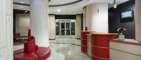 Una moderna zona de recepción con un mostrador curvo, una zona de estar roja y una entrada por puerta de cristal.