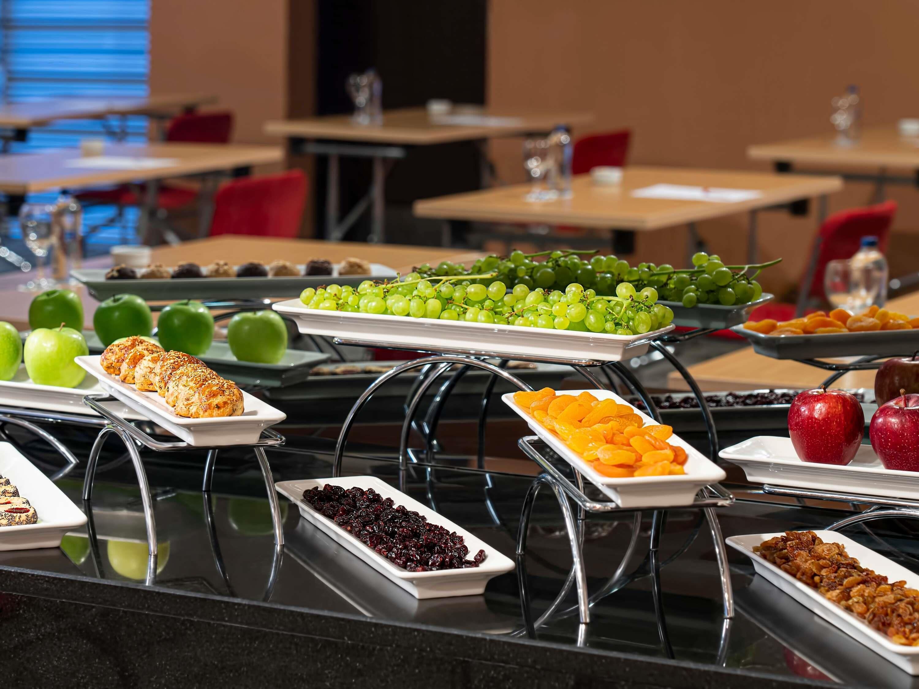 Un buffet proposant une variété d’aliments, notamment des raisins, des pommes et des pâtisseries.