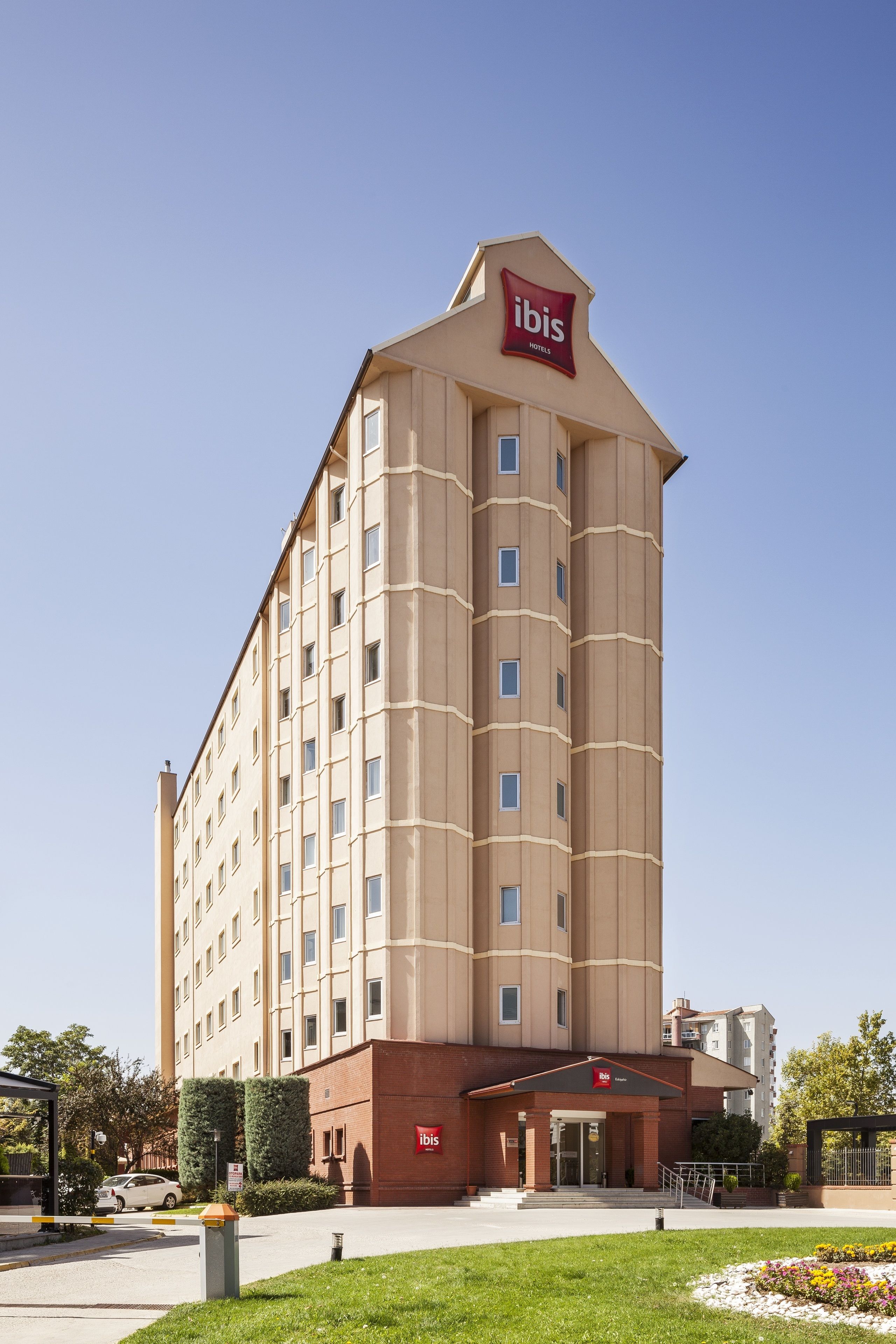 A tall, beige hotel with a red 'ibis' sign, featuring a modern design with a flat roof and large windows.