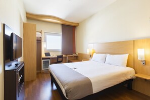 A hotel room with a large bed, a desk with a computer, a television, and a wardrobe.