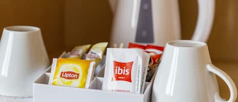Un plateau avec deux tasses blanches, une théière blanche et divers produits pour le petit-déjeuner, notamment du thé Lipton et des produits de la marque de l’hôtel Ibis.
