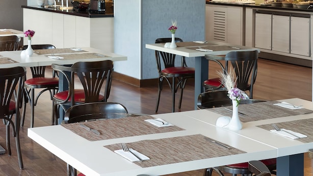Un interior de restaurante moderno con techo de ladrillo, mesas blancas y sillas con cojines rojos.