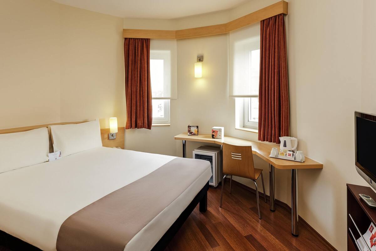 Une chambre d’hôtel avec un grand lit, un bureau, une chaise, une télévision et une petite table sur laquelle se trouve une machine à café.