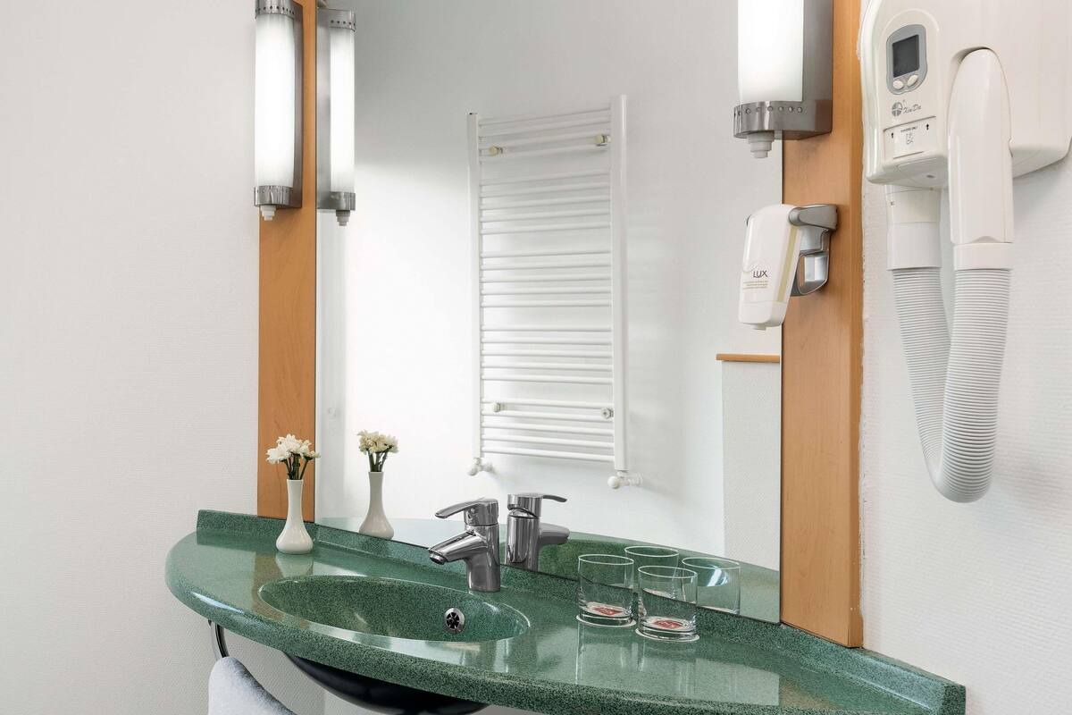 Une salle de bain moderne avec un lavabo en granit vert, un miroir, un porte-serviettes, une douchette à main et un téléphone fixé au mur.