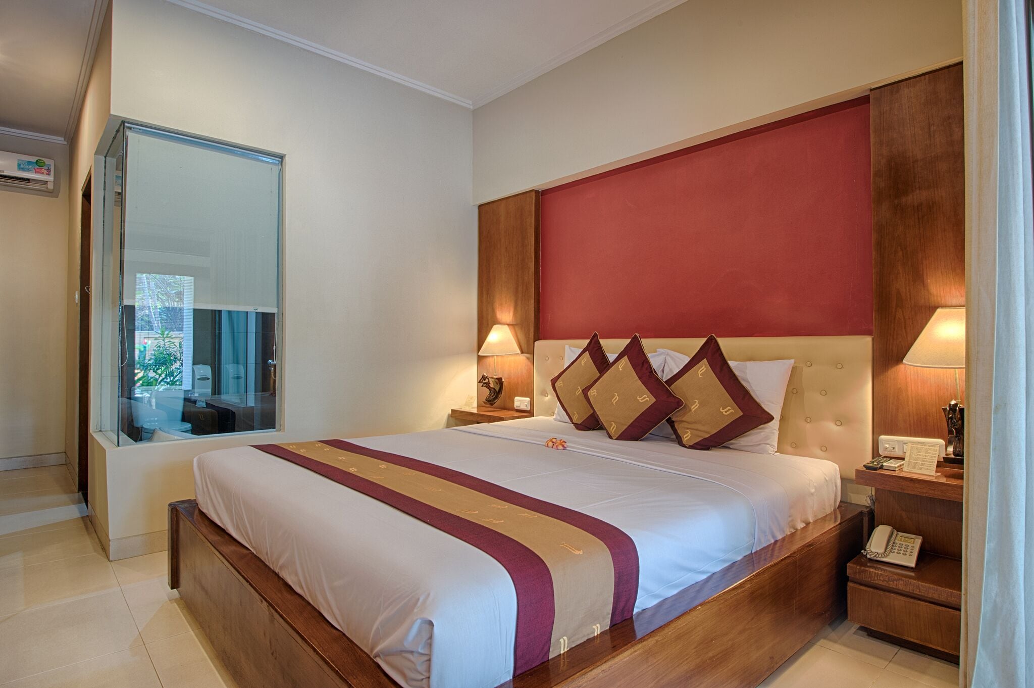 A hotel room with a large bed, wooden headboard, two bedside tables with lamps, a mirror, and a small bedside table with a phone.