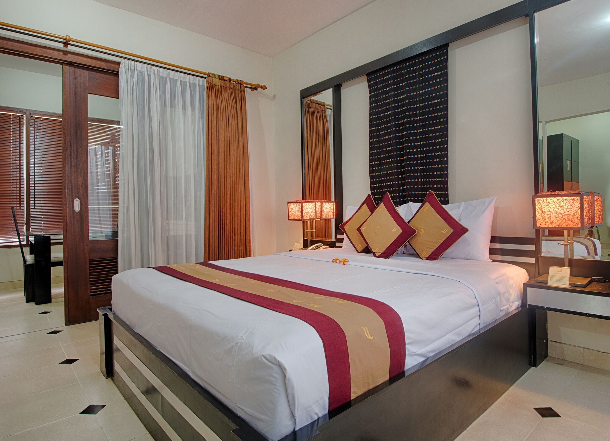 A hotel room with a large bed, a wooden wardrobe, a mirror, and a window with curtains.