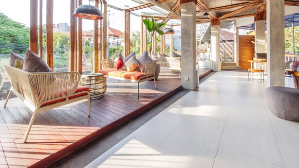 Un interior espacioso y moderno con grandes ventanales, vigas de madera y una variedad de zonas de estar, incluyendo un sofá y sillones.