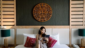 Habitación de hotel con cama, almohadas, un adorno en la pared y dos mesitas de noche con lámparas y un teléfono.