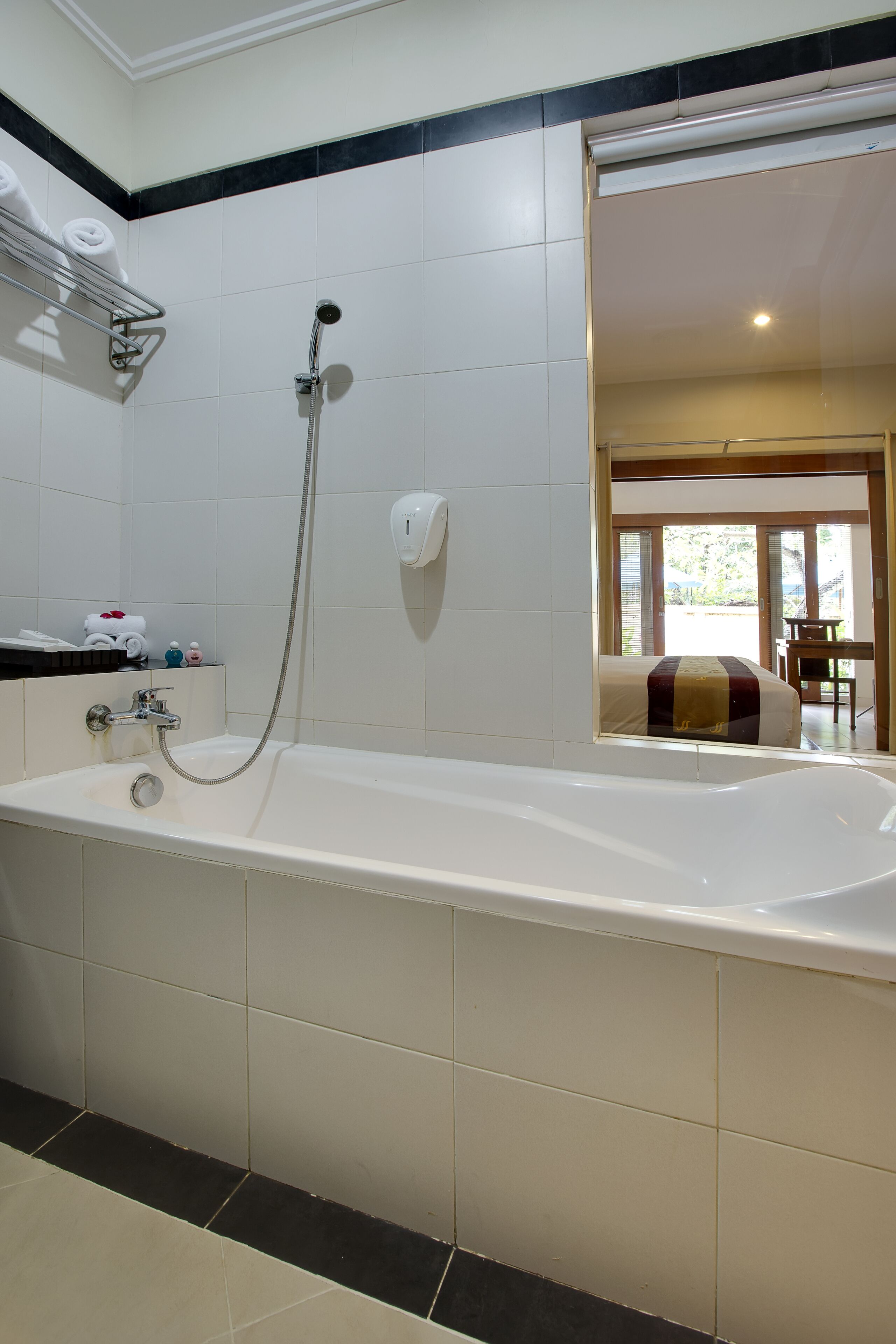 Un baño con bañera, ducha e inodoro. Hay un perchero con toallas y artículos de aseo.