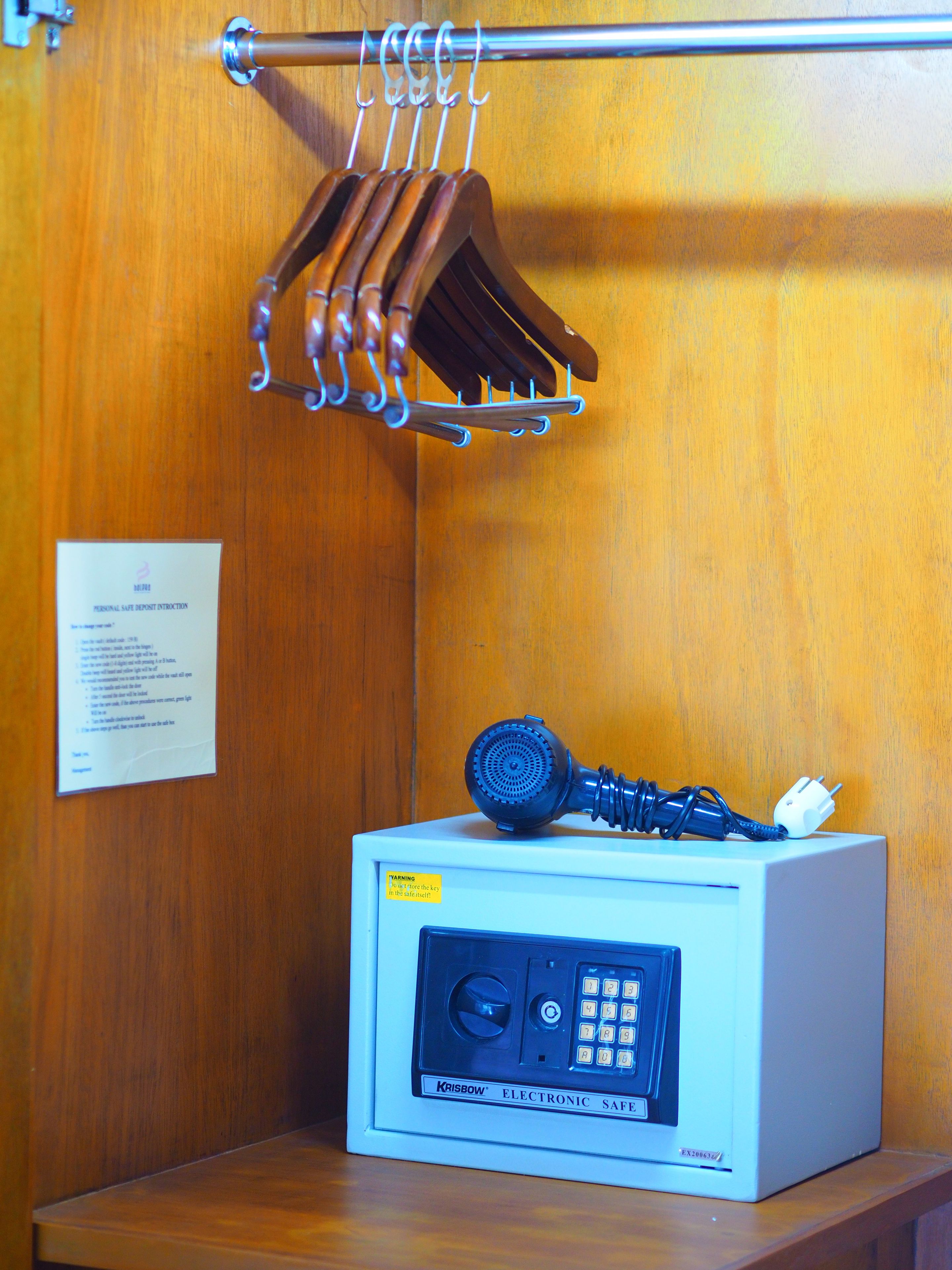 Eine Holztür mit einem Metallkleiderhaken, an dem braune Holzkleiderbügel hängen. Ein weißer elektronischer Safes mit Tastatur und Telefon steht auf einer Holzfläche.