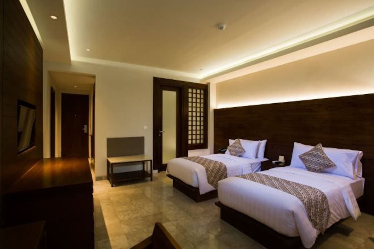 A hotel room with two beds, a TV, and a wooden headboard.