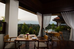 A dining area with a table set for two, surrounded by chairs, overlooking a scenic view with mountains and greenery.