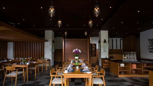 Een restaurant met een geruit vloertje, houten tafels en stoelen, hangende pendantlampen en een bloemstuk in het midden.