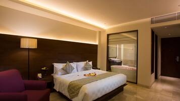 A hotel room with a large bed, a nightstand, a red armchair, a bathroom with a bathtub, and a mirror.