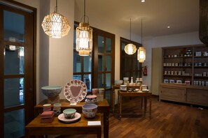 A room with wooden flooring, a dining table with various bowls and plates, hanging wicker lamps, and a cabinet with jars.