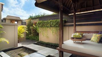 A modern outdoor seating area with a stone-tiled floor, a small water feature, and a wooden pergola.