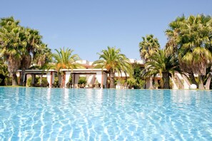 Une piscine d’eau cristalline, entourée de palmiers, et un bâtiment doté d’un espace de repos abrité.
