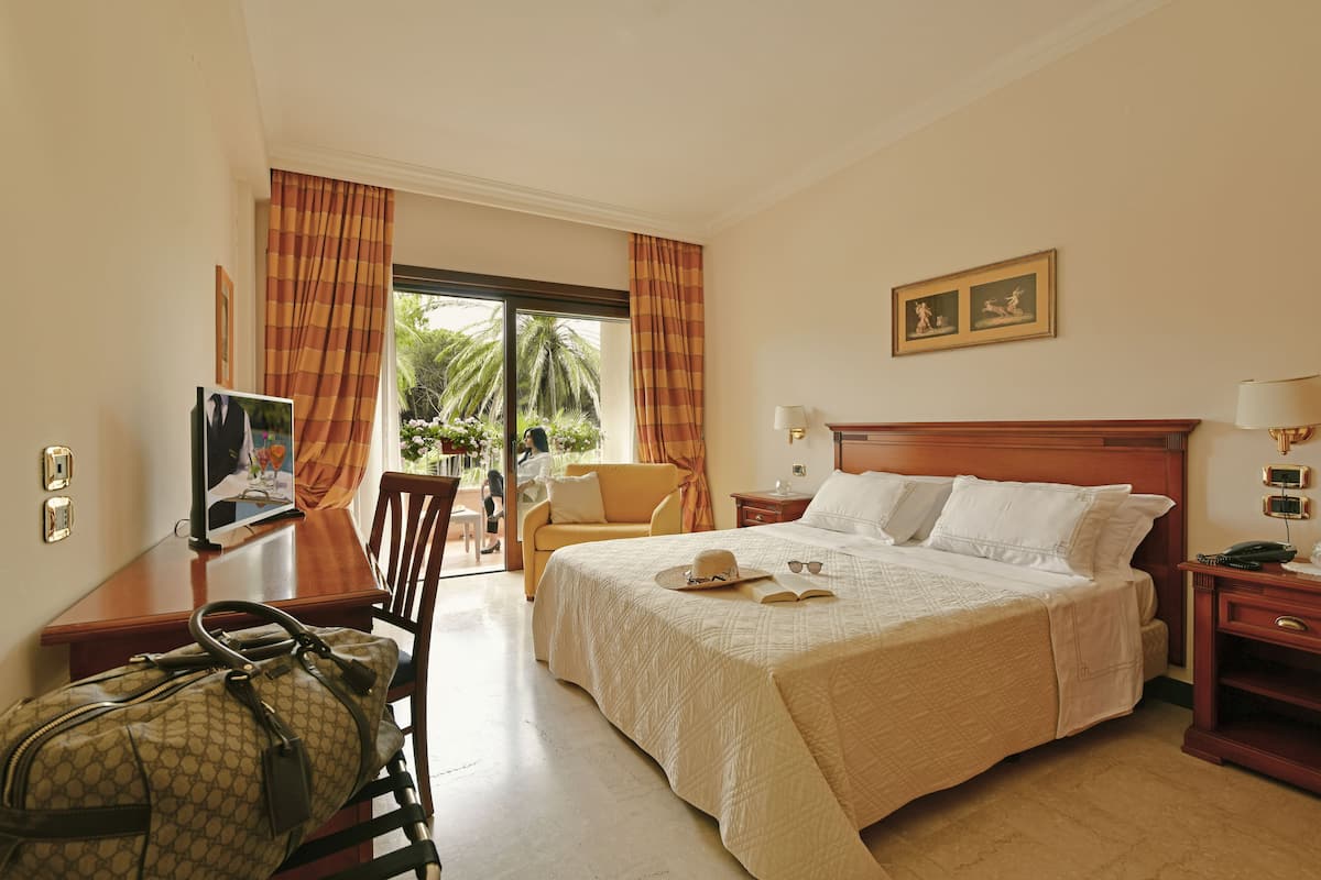Ein Hotelzimmer mit einem großen Bett, einem Schreibtisch, einem Stuhl und Blick ins Freie.