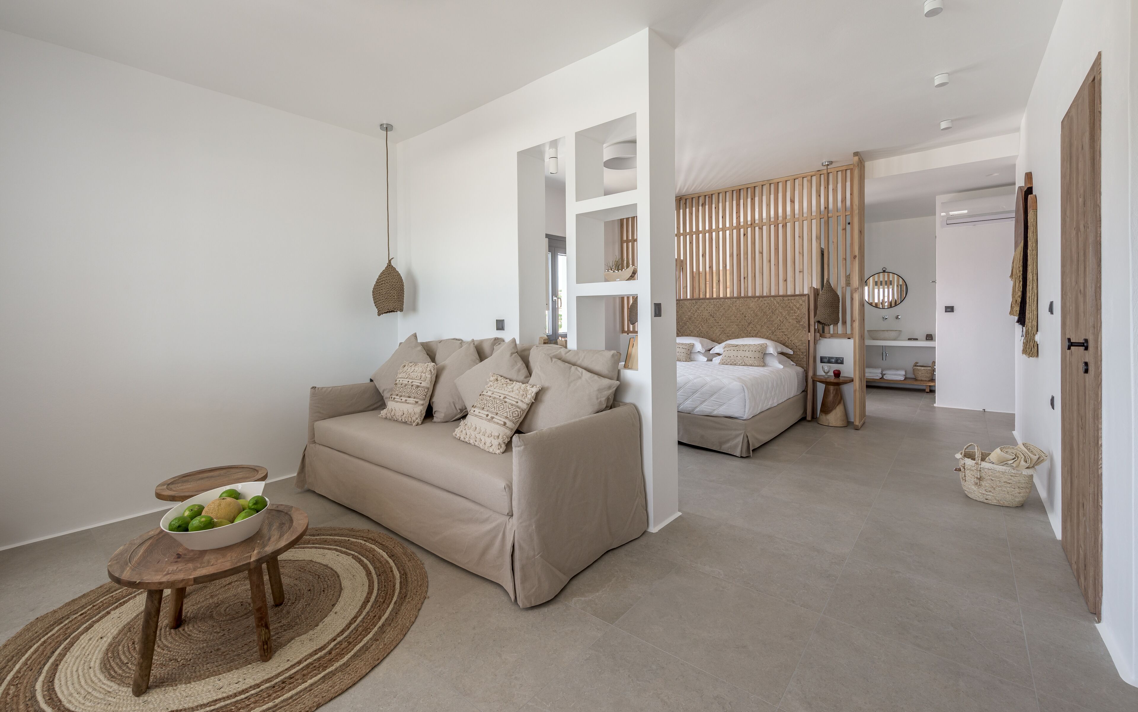 A modern, minimalist bedroom with a sofa, a bed, and a small table with fruit.