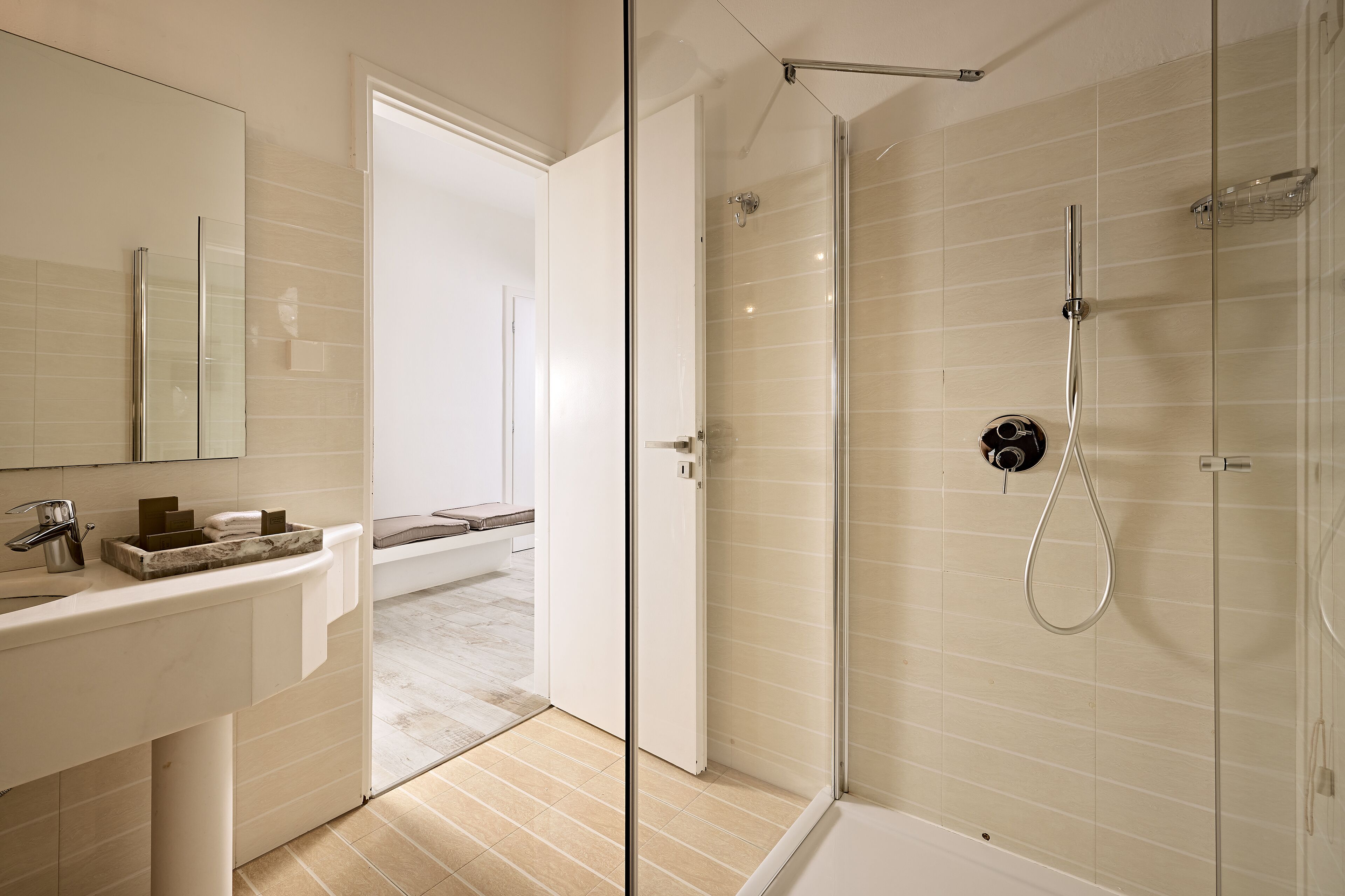 A modern bathroom with a glass-enclosed shower, a white sink with a marble countertop, and a visible door leading to another room.