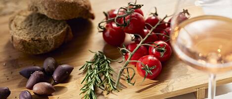 A wooden cutting board with sliced bread, cherry tomatoes, rosemary, and olives.