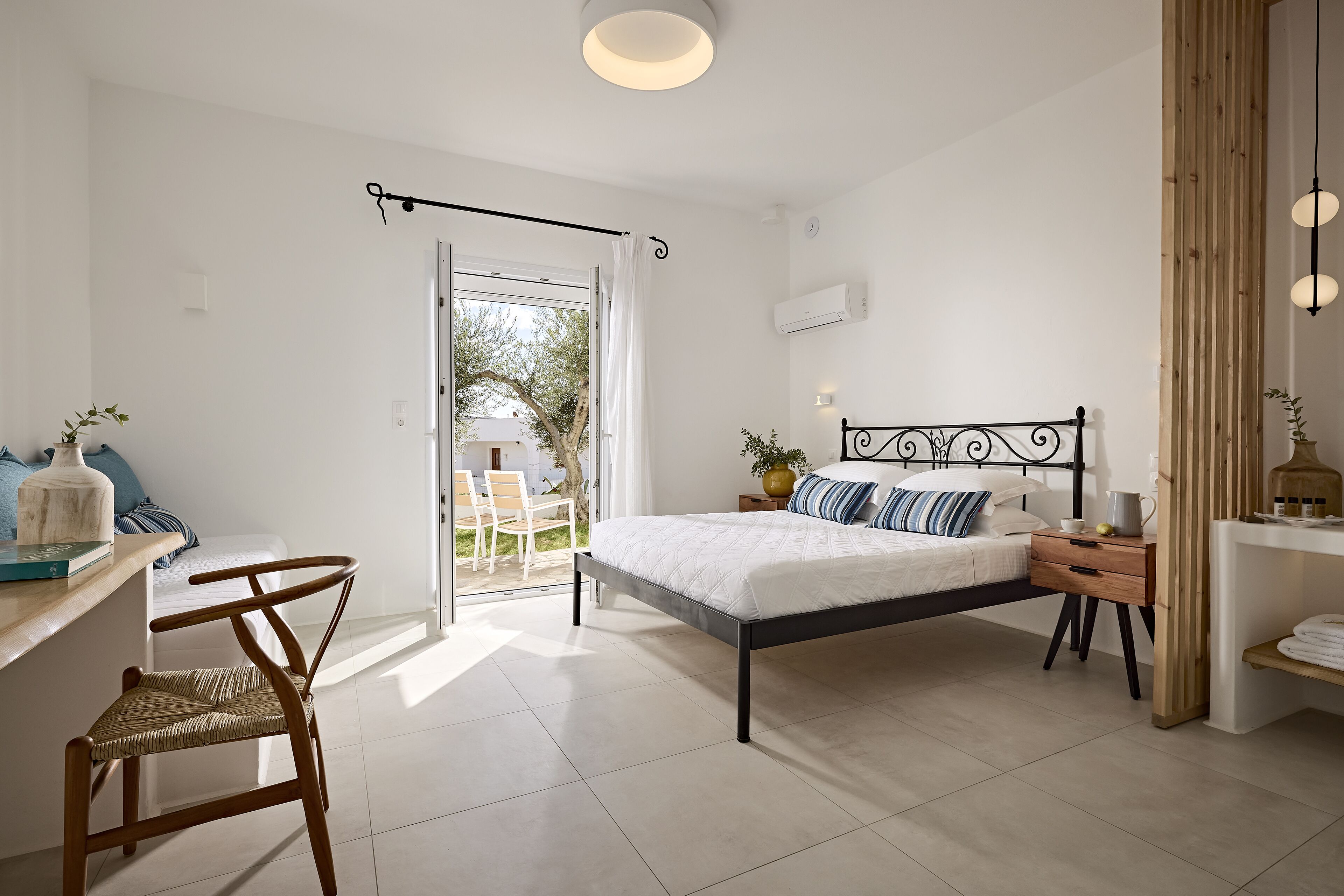 A bedroom with a bed, a desk, a chair, and a view of the outdoors.