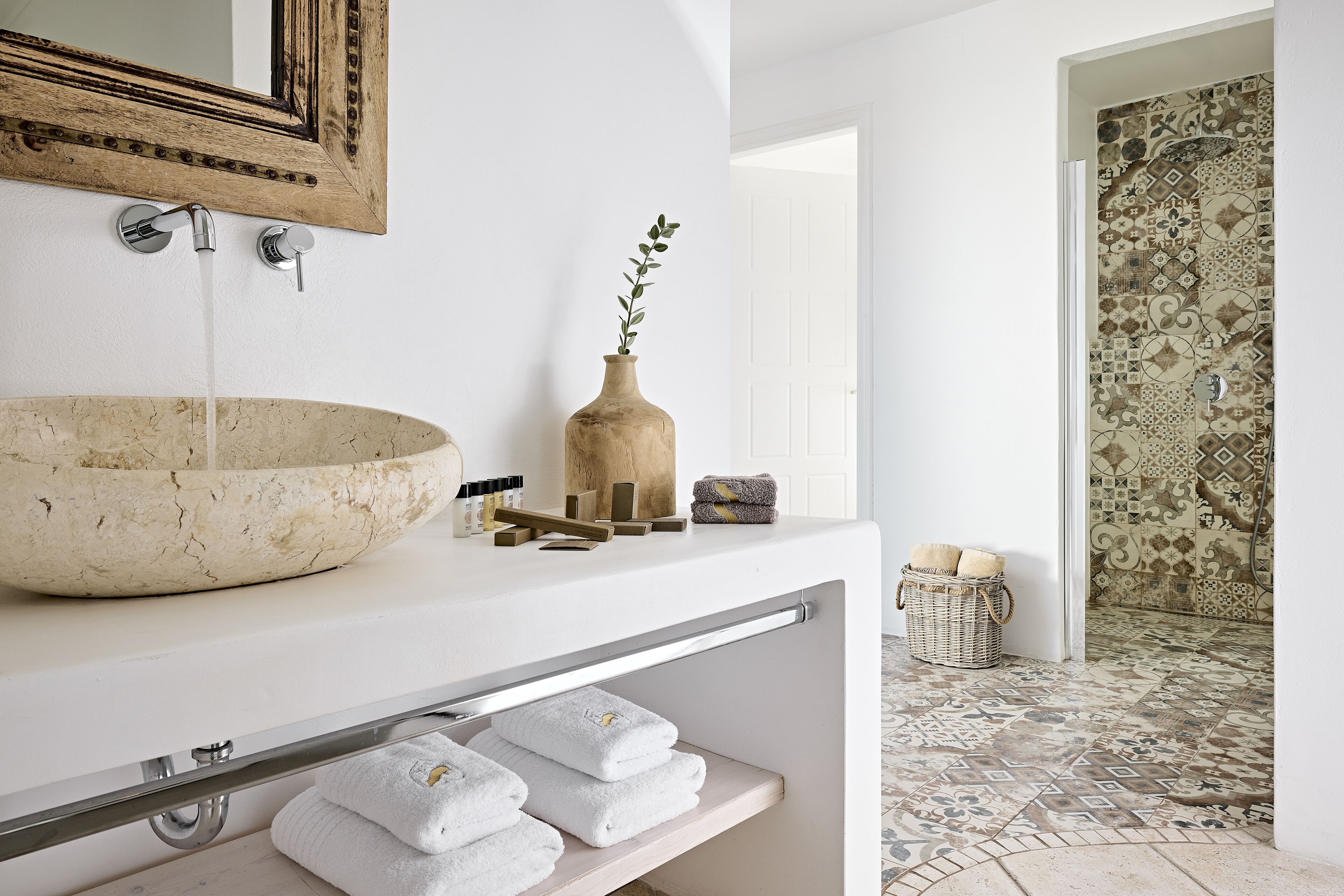 Un baño con un lavabo grande, un espejo, un florero con planta y una ducha con azulejos decorados.