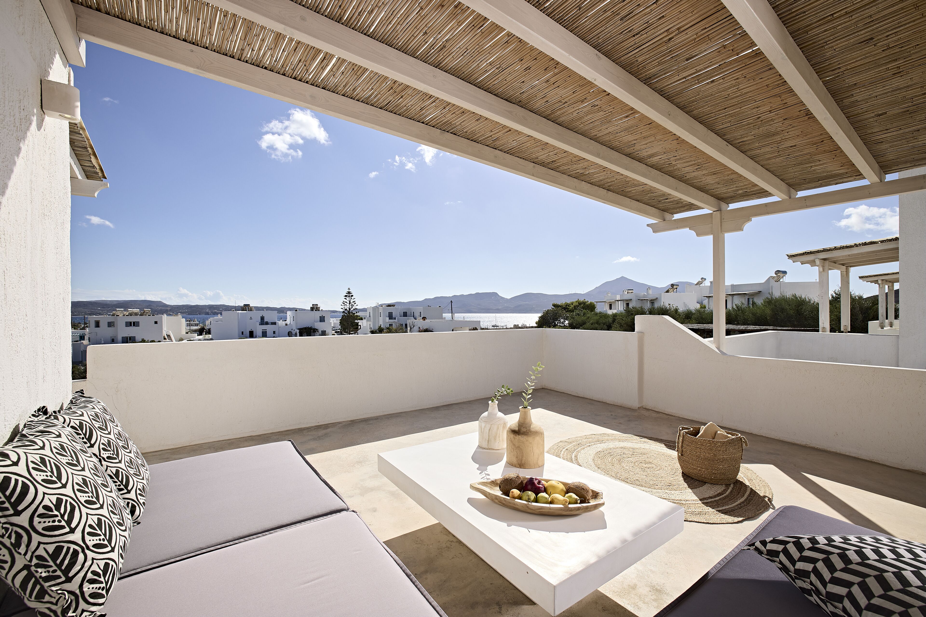 A rooftop terrace with a view of the sea, white walls, and a wooden pergola.