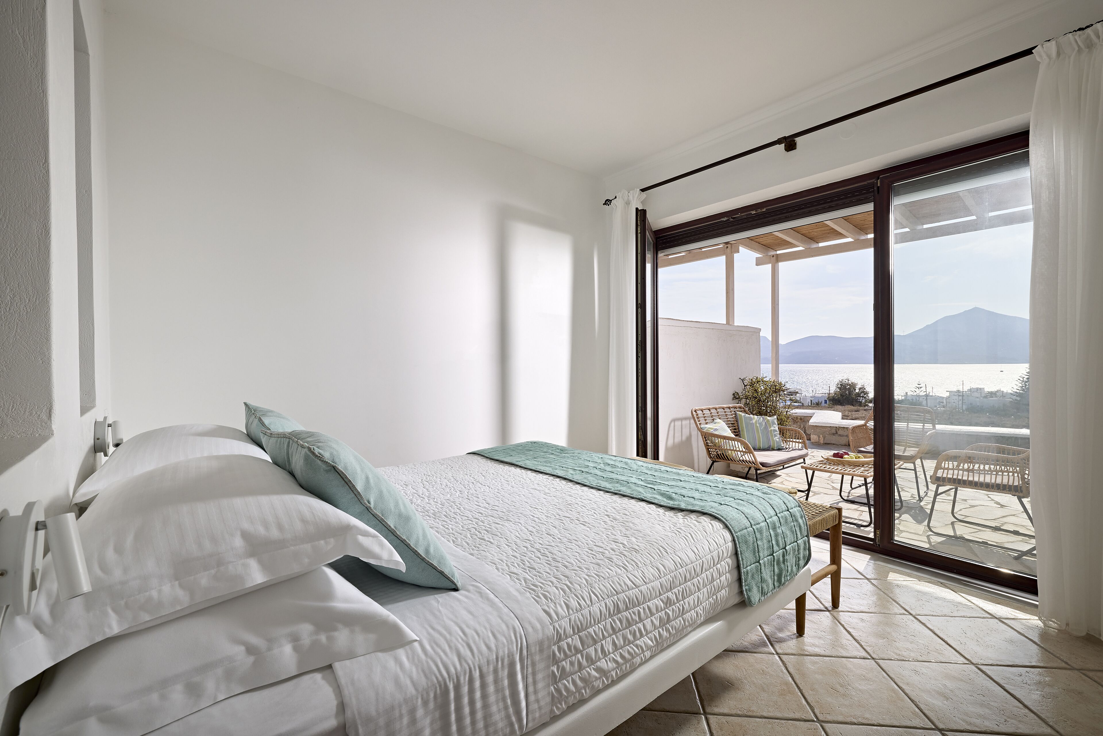 A bedroom with a bed, a view of the outdoors, and a balcony with seating.