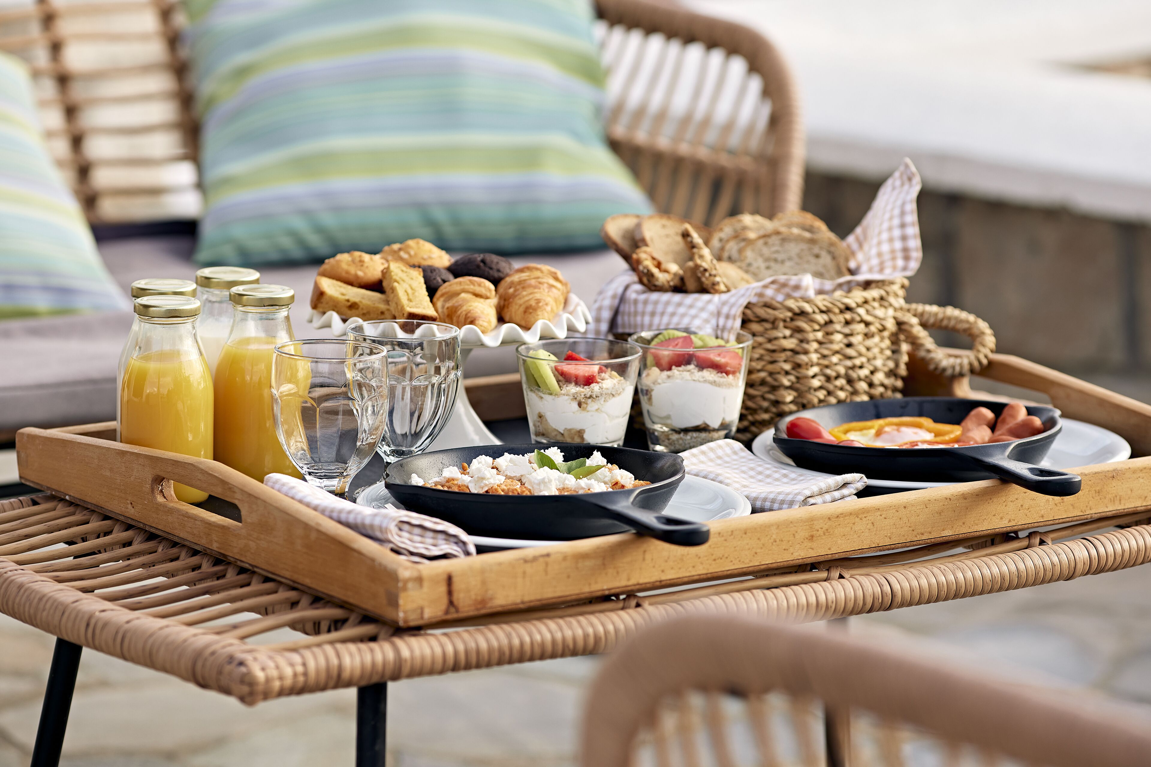 A breakfast tray with croissants, pastries, and a skillet with eggs and sausages.