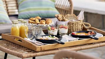 A breakfast tray with croissants, pastries, and a skillet with eggs and sausages.