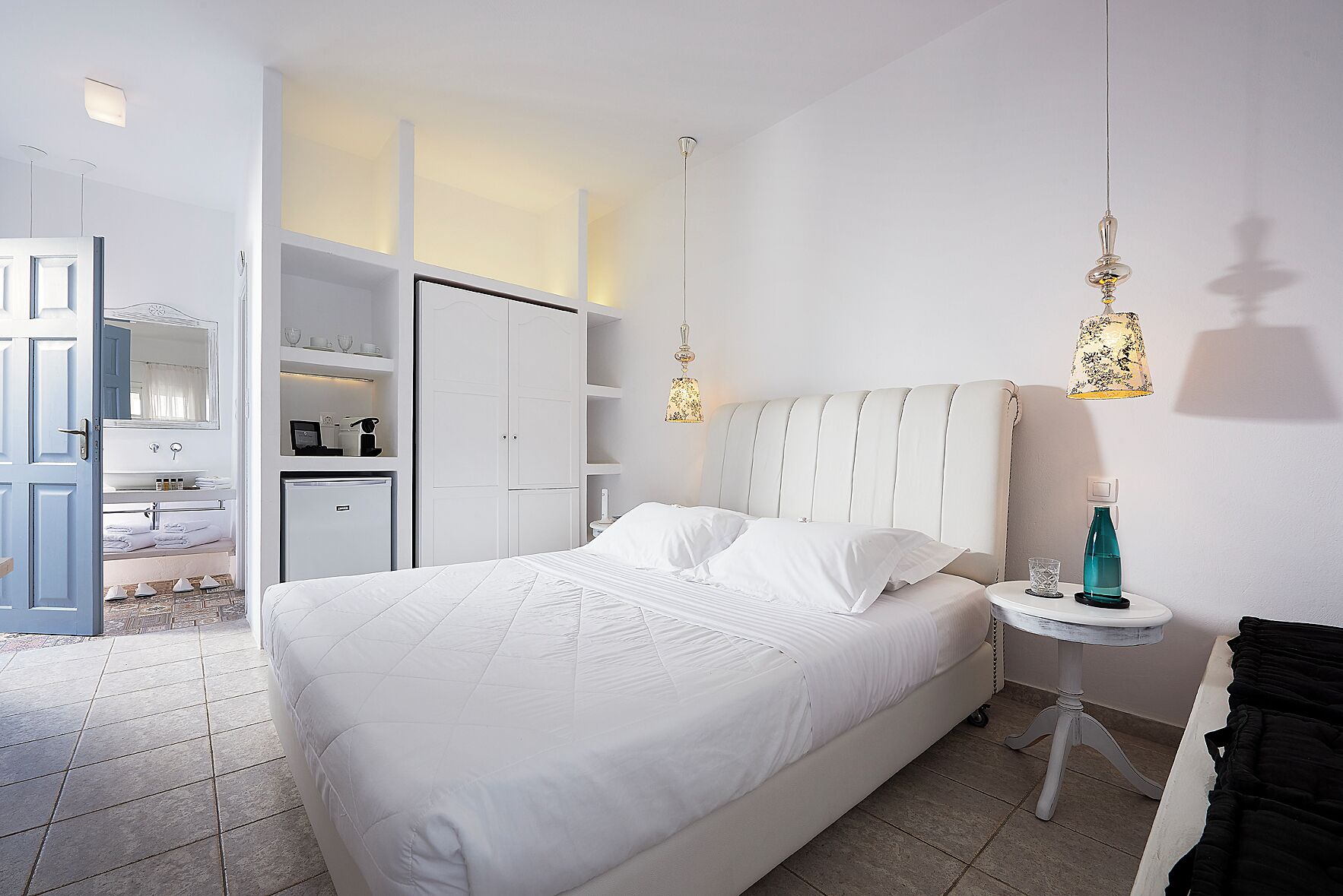 A hotel room with a bed, a wardrobe, a small table with a lamp, and a bathroom visible through an open door.