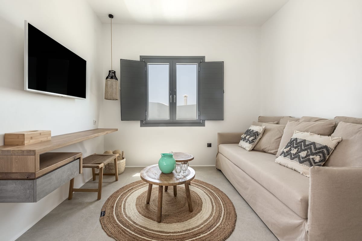 Ein modernes Wohnzimmer mit Flachbildfernseher, einer Couch, einem Couchtisch und einem Fenster mit Rollläden.