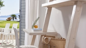 Un espacio interior blanco con vistas al exterior, una mesa blanca con un florero y un libro, y una bolsa de papel marrón.