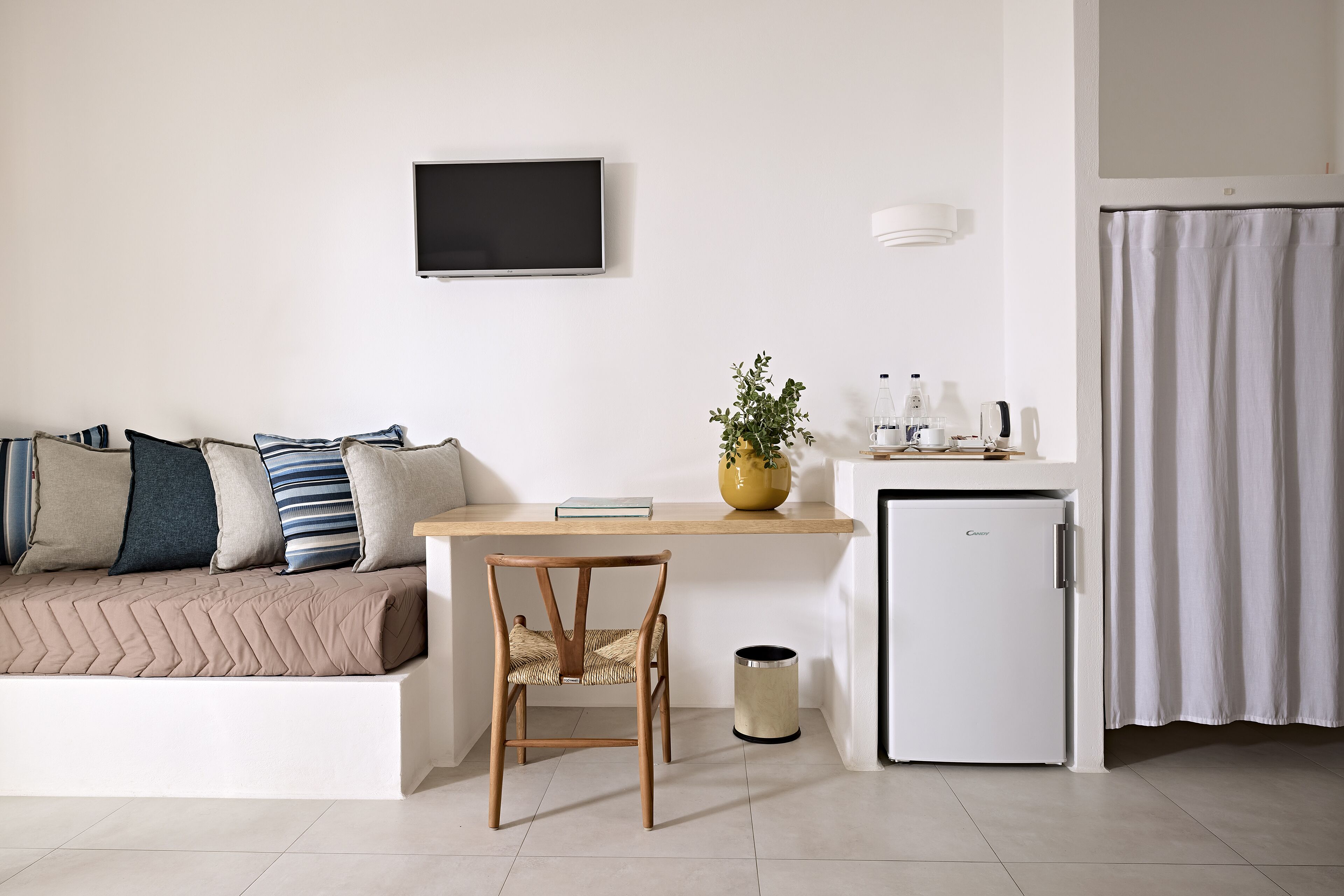 Una sala de estar moderna con un sofá, una silla de madera, una mesita con una planta, un televisor y un refrigerador pequeño.