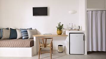 Una sala de estar moderna con un sofá, una silla de madera, una mesita con una planta, un televisor y un refrigerador pequeño.