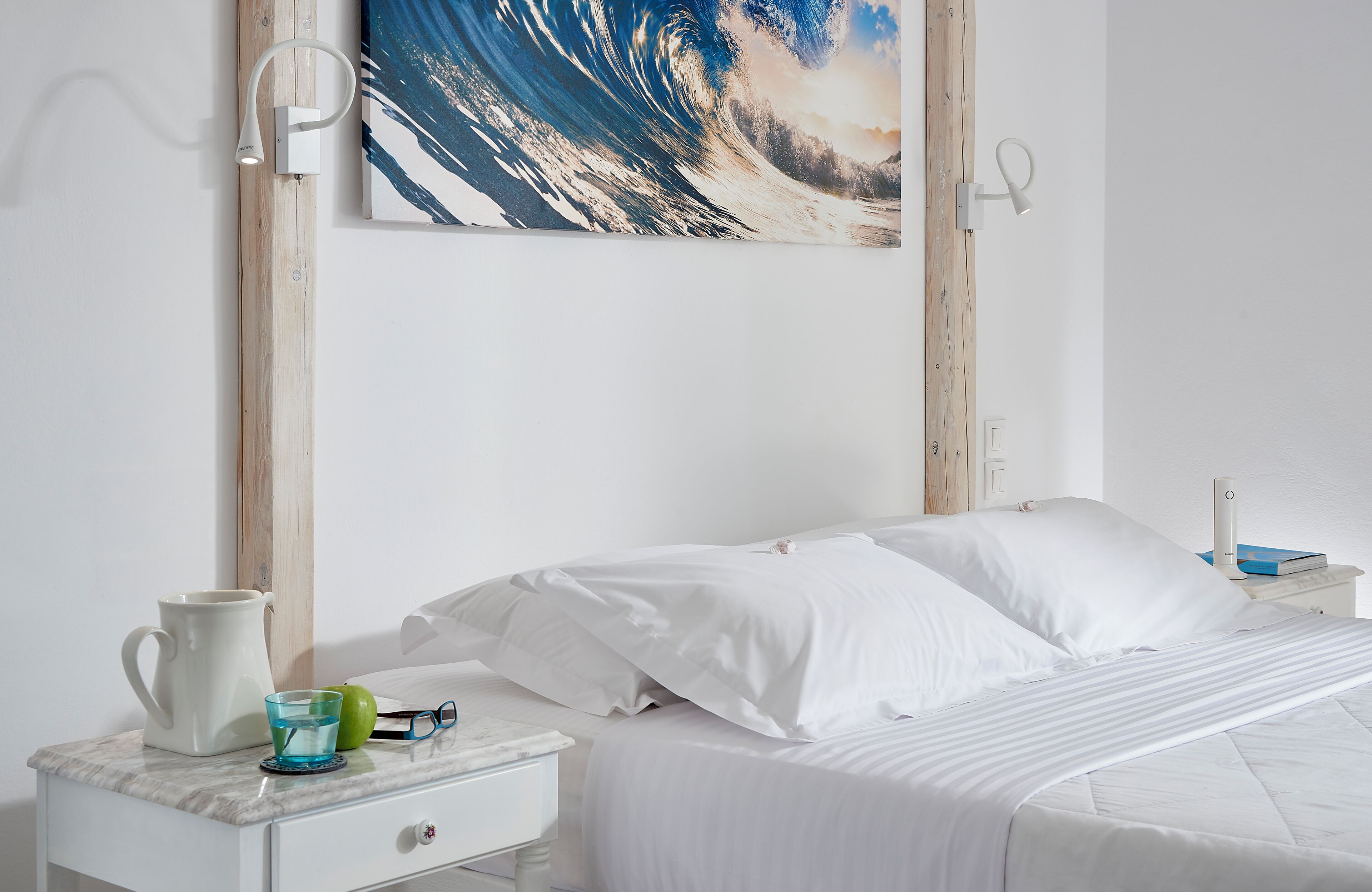 A bedroom with a bed, white bedding, a nightstand with a lamp, a pitcher, and a glass.