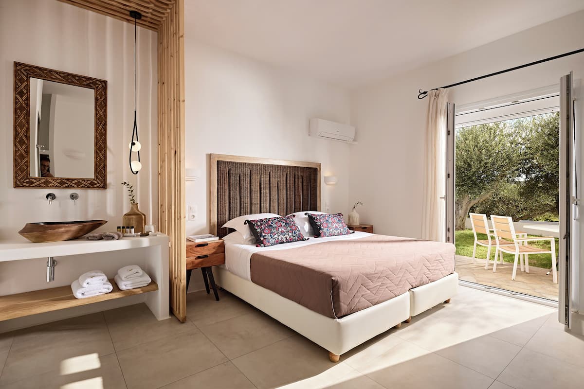 Ein Schlafzimmer mit Bett, Nachttischen, einem Spiegel, einem Fenster und Blick ins Freie.