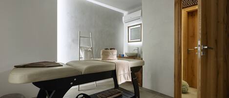 A modern spa room with a massage table, a small sink, and a wooden door.