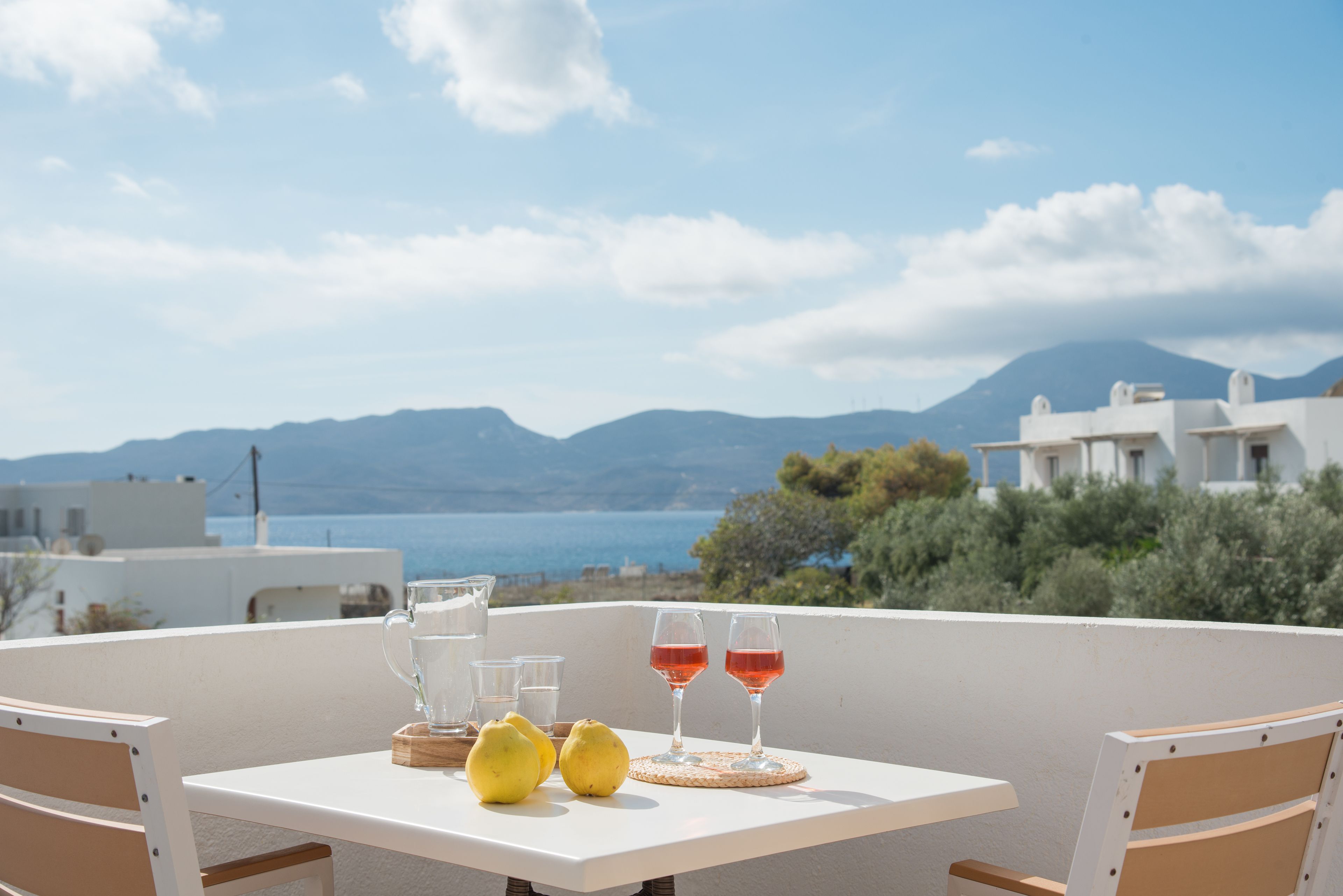 Een tafel met glazen en citroenen op een balkon met uitzicht op zee en bergen.