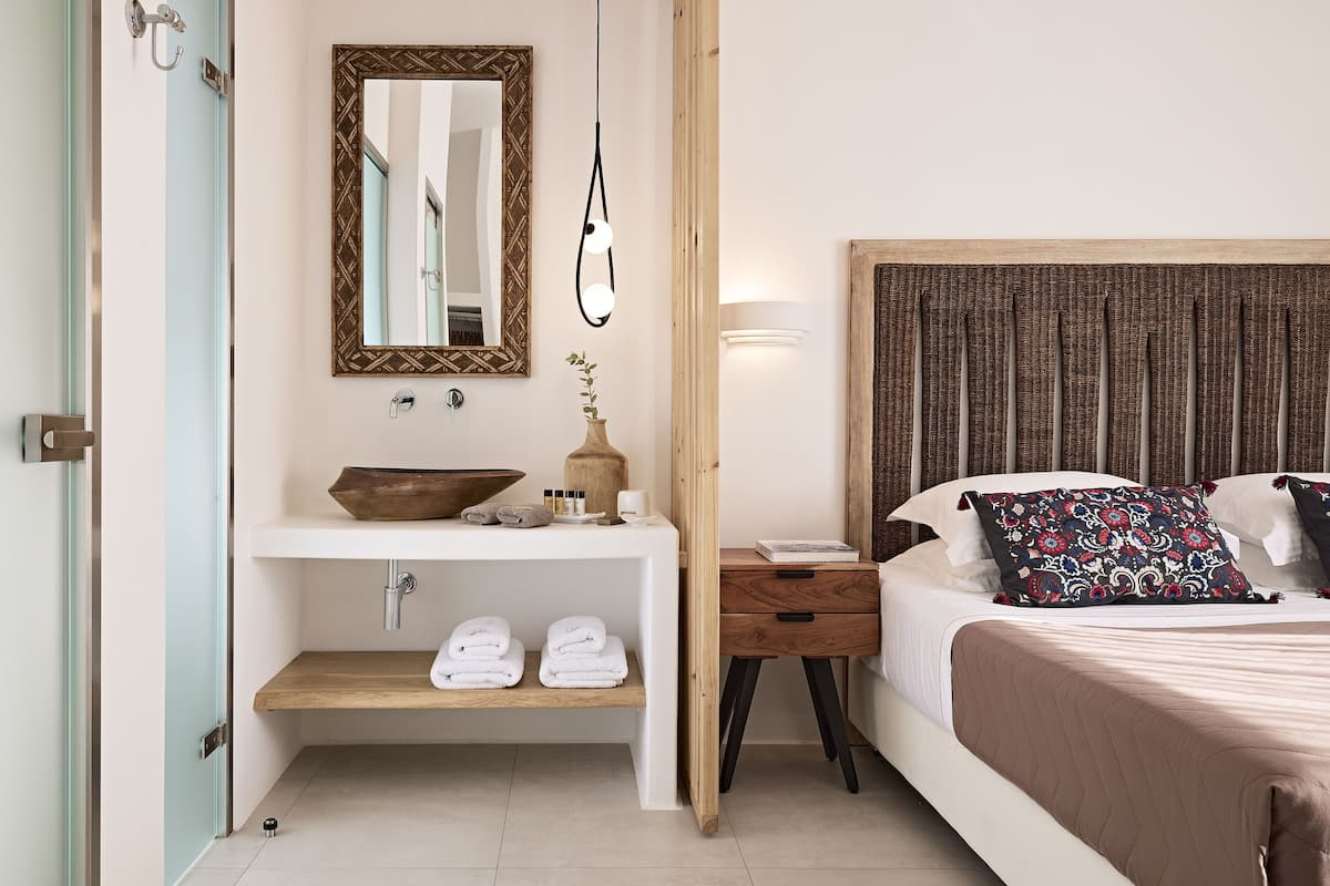 Ein Schlafzimmer mit einem Holz-Kopfteil, einem Nachttisch mit Lampe, einem Spiegel und einem Regal mit Handtüchern und Toilettenartikeln.