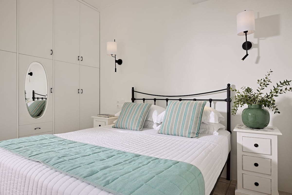 Ein ordentlich eingerichtetes Schlafzimmer mit Bett, Nachttischen, einem Spiegel und einer Wandlampe.