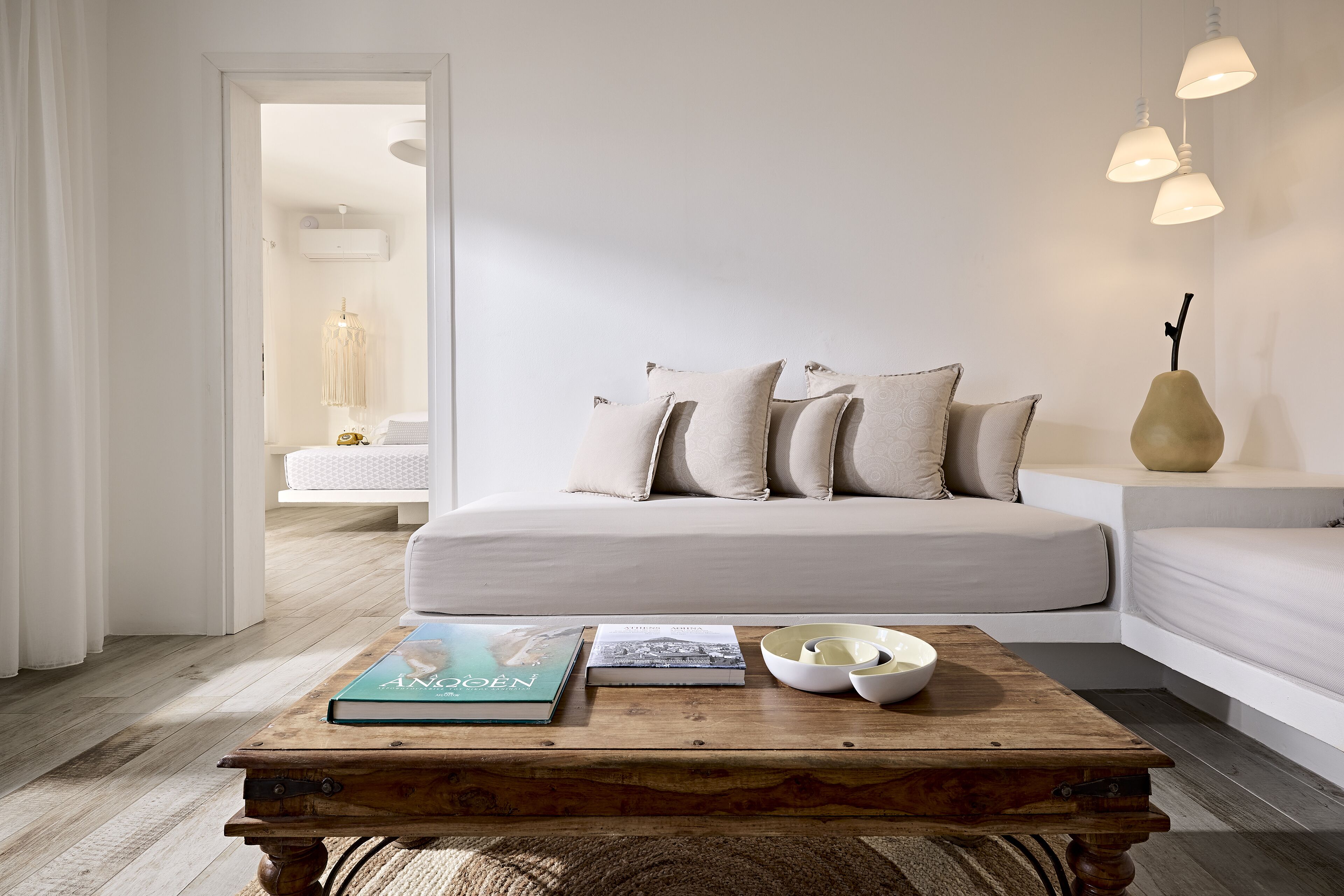 Une chambre à coucher moderne avec un grand lit, une table basse en bois sur laquelle sont posés des livres et des bols, et une table de chevet agrémentée d’un vase.