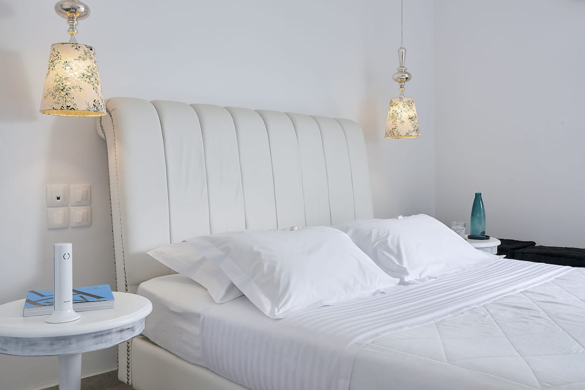Ein ordentlich bezogenes Bett mit weißen Leinen, ein Nachttisch mit Lampe und eine Wandleuchte.