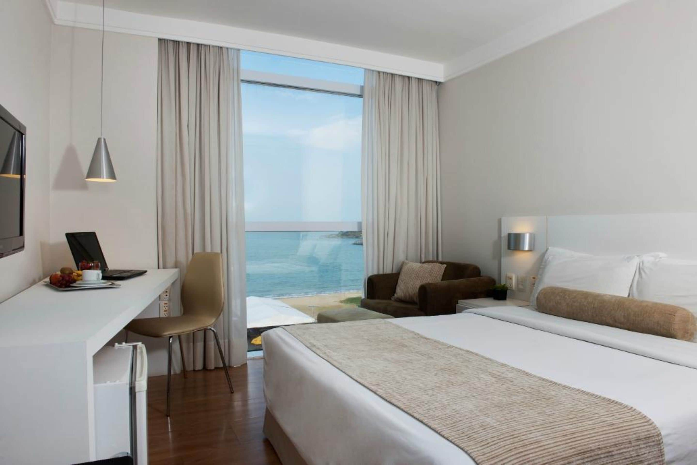 Una habitación de hotel con una cama, un escritorio, una silla, un sofá y un ventanal con vistas al mar.