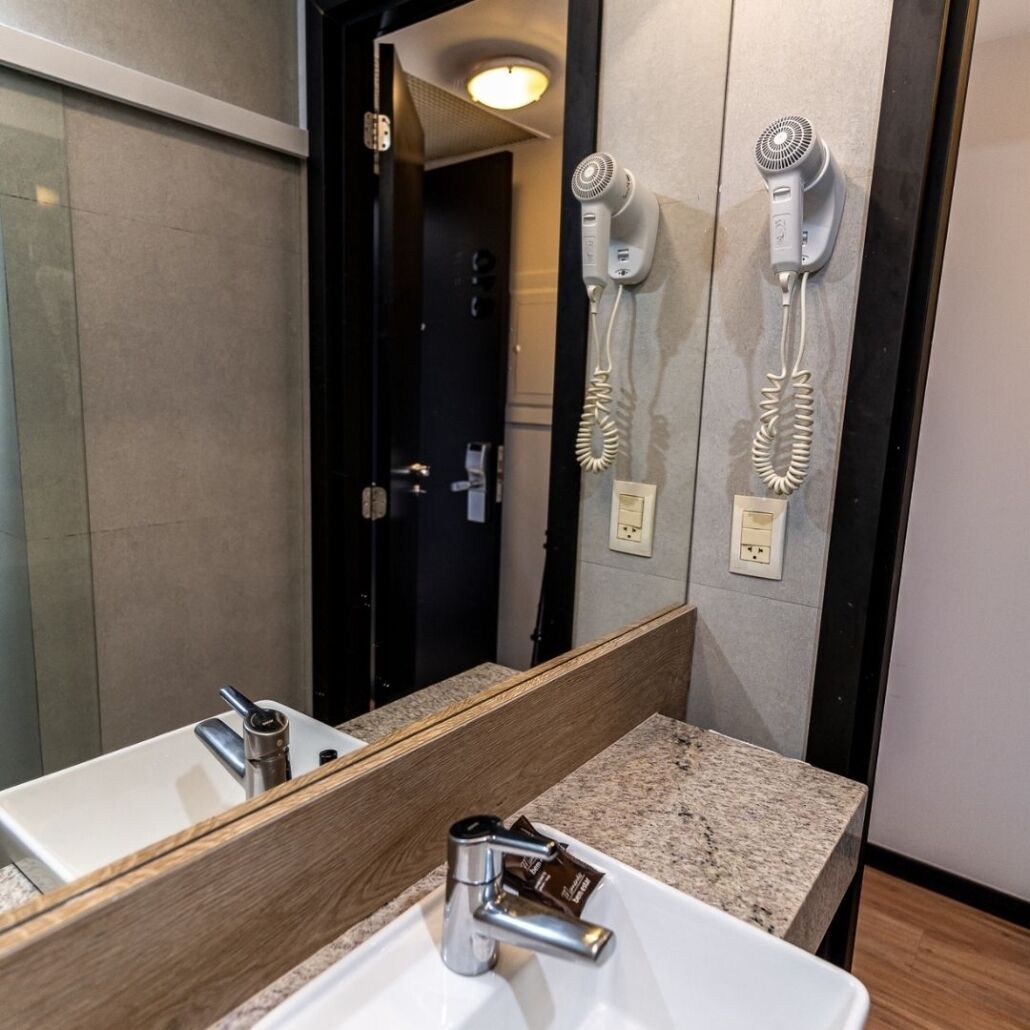 Un baño moderno con un espejo grande, un lavamanos y dos secadores de pelo fijados en la pared.