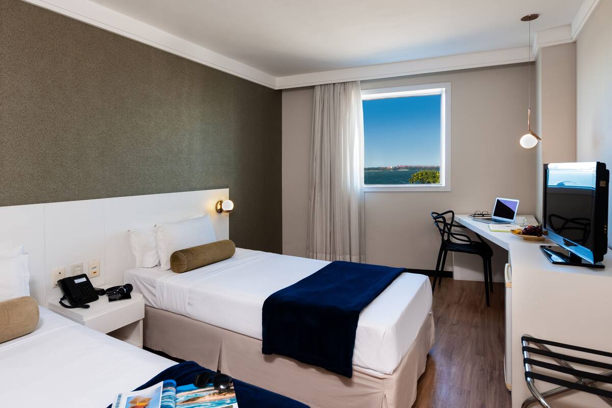 Ein Hotelzimmer mit zwei Betten, einem Schreibtisch mit Computer, einem Stuhl und einem Fenster mit Blick.
