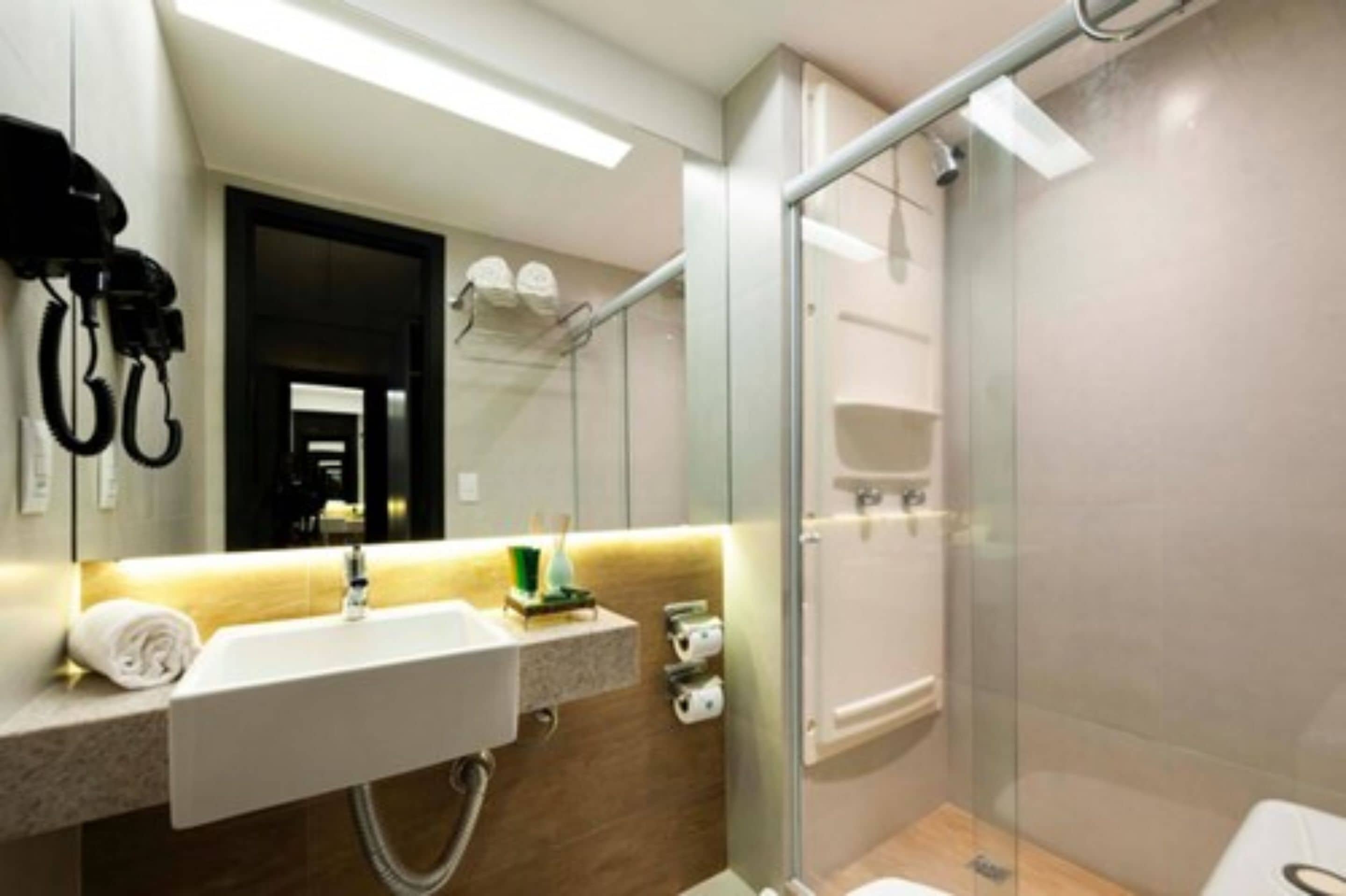 Un baño moderno con cabina de ducha de vidrio, un lavabo blanco con una toalla y un espejo.
